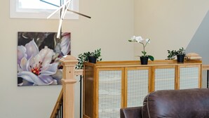 Un espace d’accueil avec un bureau en bois, des plantes en pot, un tableau floral encadré et un escalier.