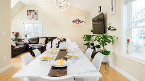 Un coin repas avec une longue table dressée pour un repas, un canapé en cuir marron et un tableau représentant un paysage urbain accroché au mur.