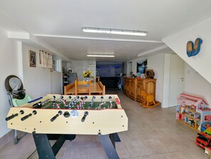 Una habitación con mesa de futbolín, mesa de comedor y zona de juegos para niños.