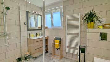 A modern bathroom with a glass shower enclosure, a white towel rack, and a potted plant.