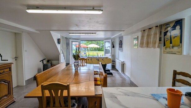 Een eetgedeelte met een lange houten tafel, stoelen en een marmeren aanrecht.