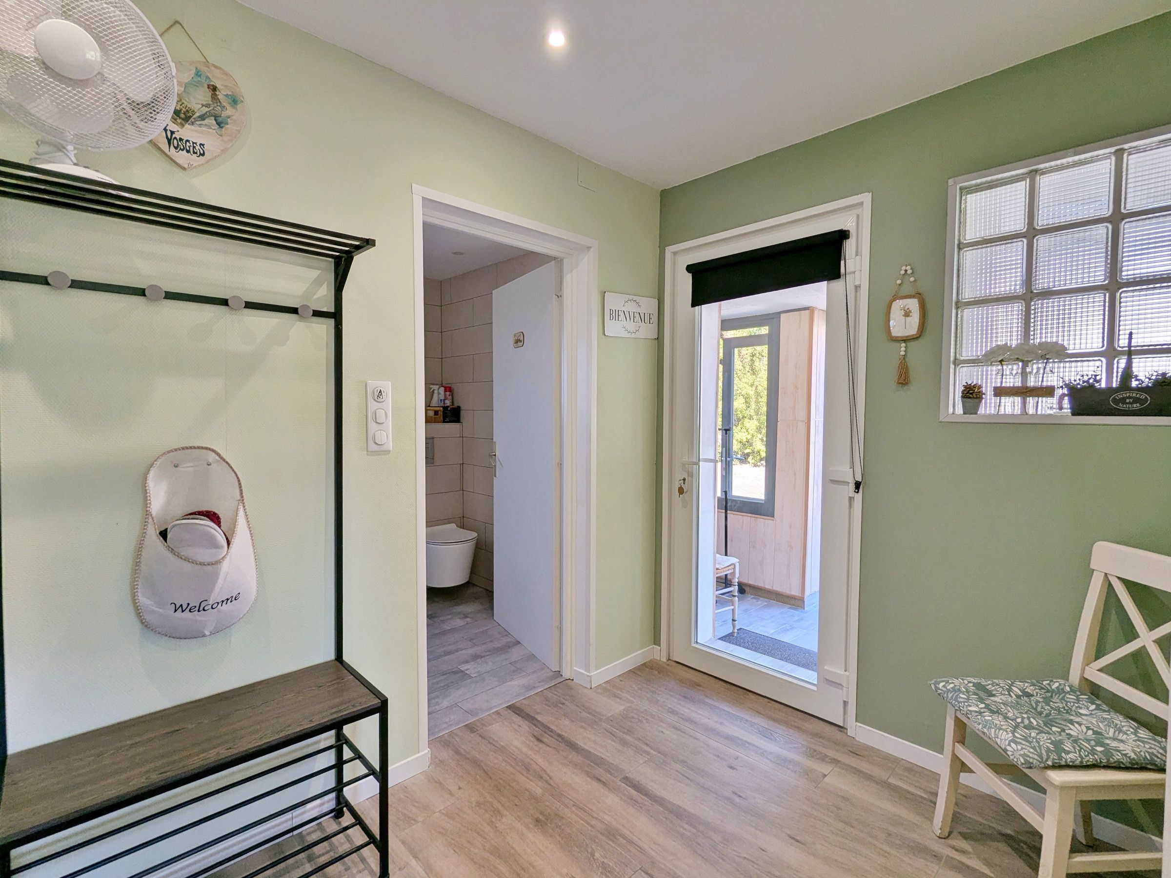 A room with a wooden floor, a white door leading to a bathroom, a bench, and a fan on the wall.