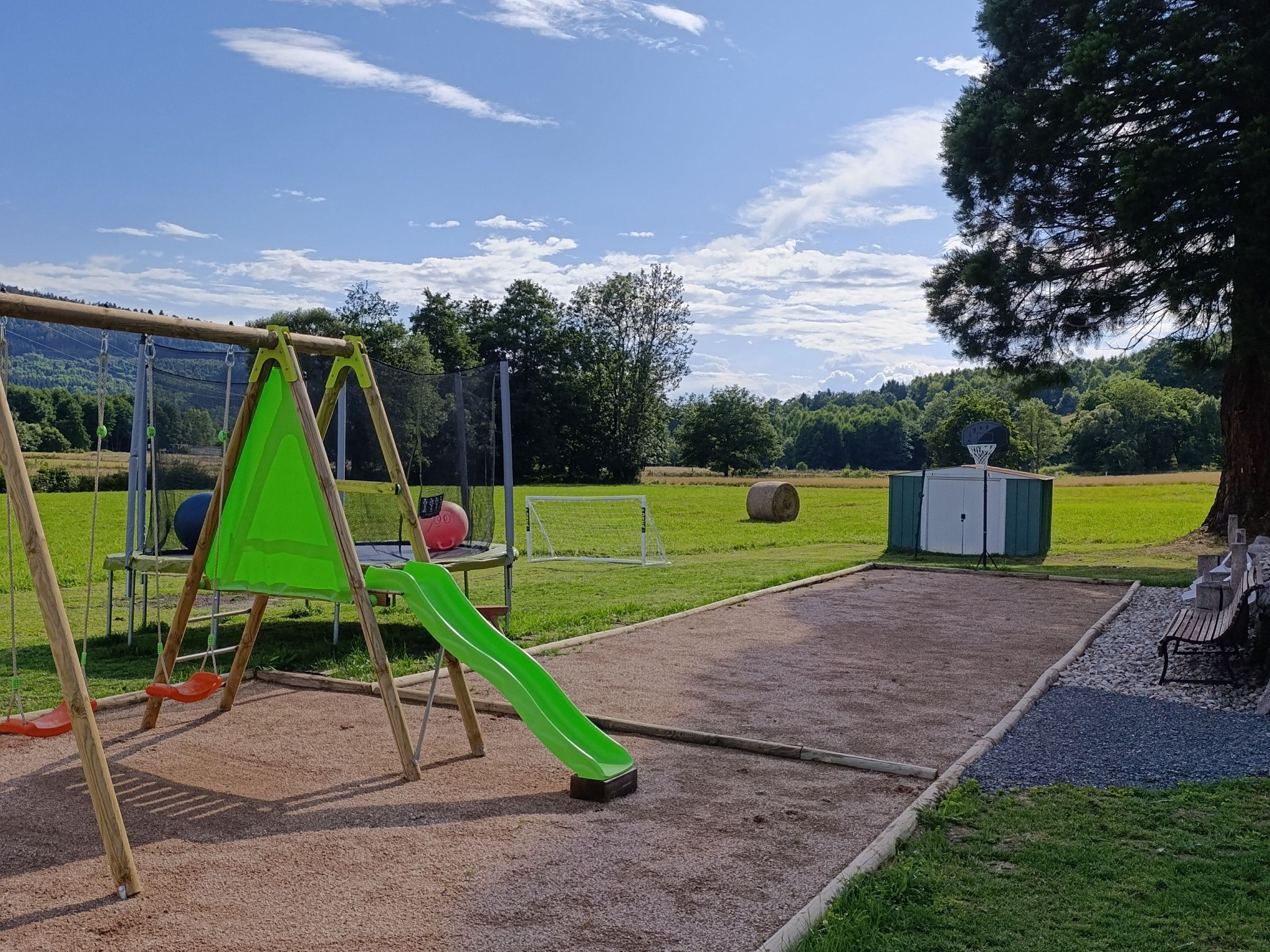Une aire de jeux avec des balançoires et un toboggan, entourée d’un champ d’herbe et d’arbres.