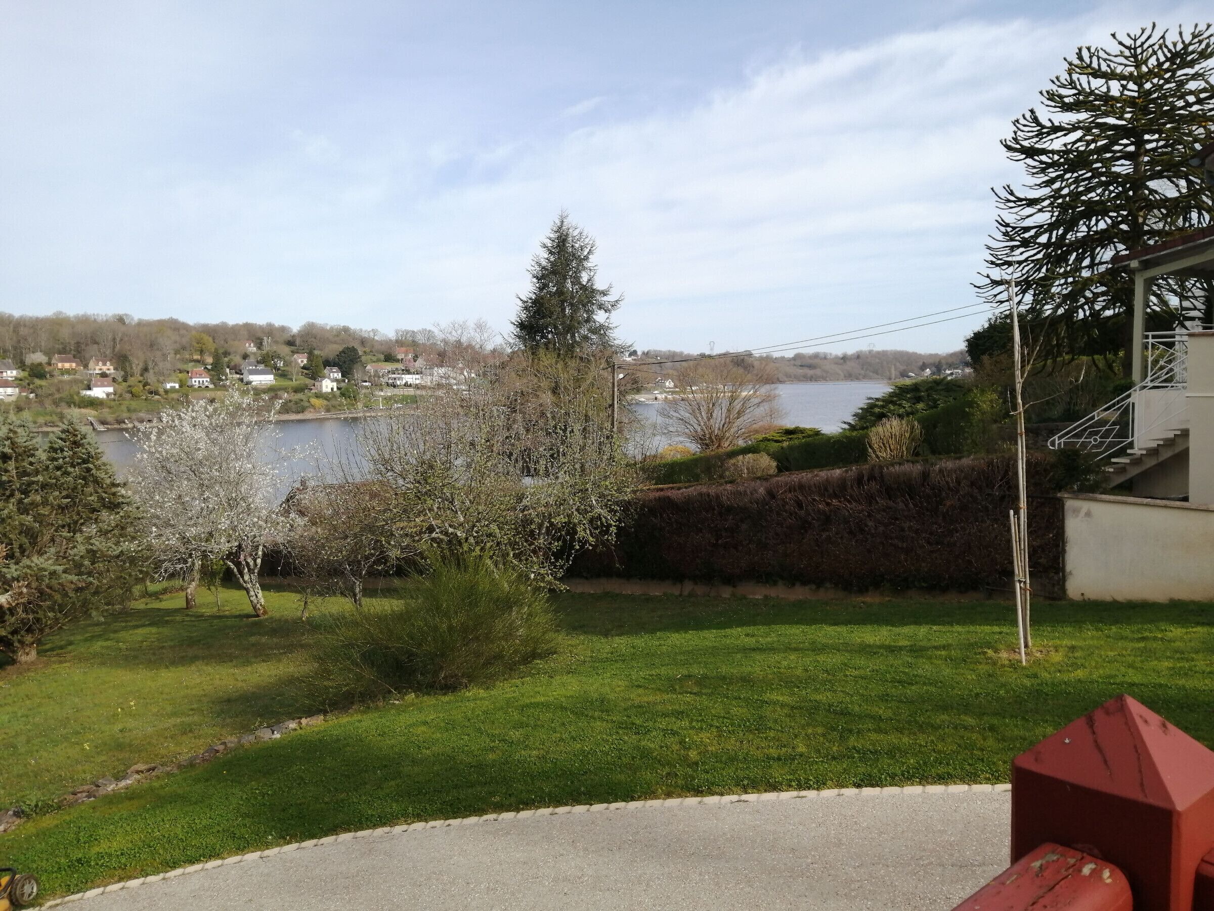 A residential area with a lawn, a red fire hydrant, and a view of a lake with houses in the background.