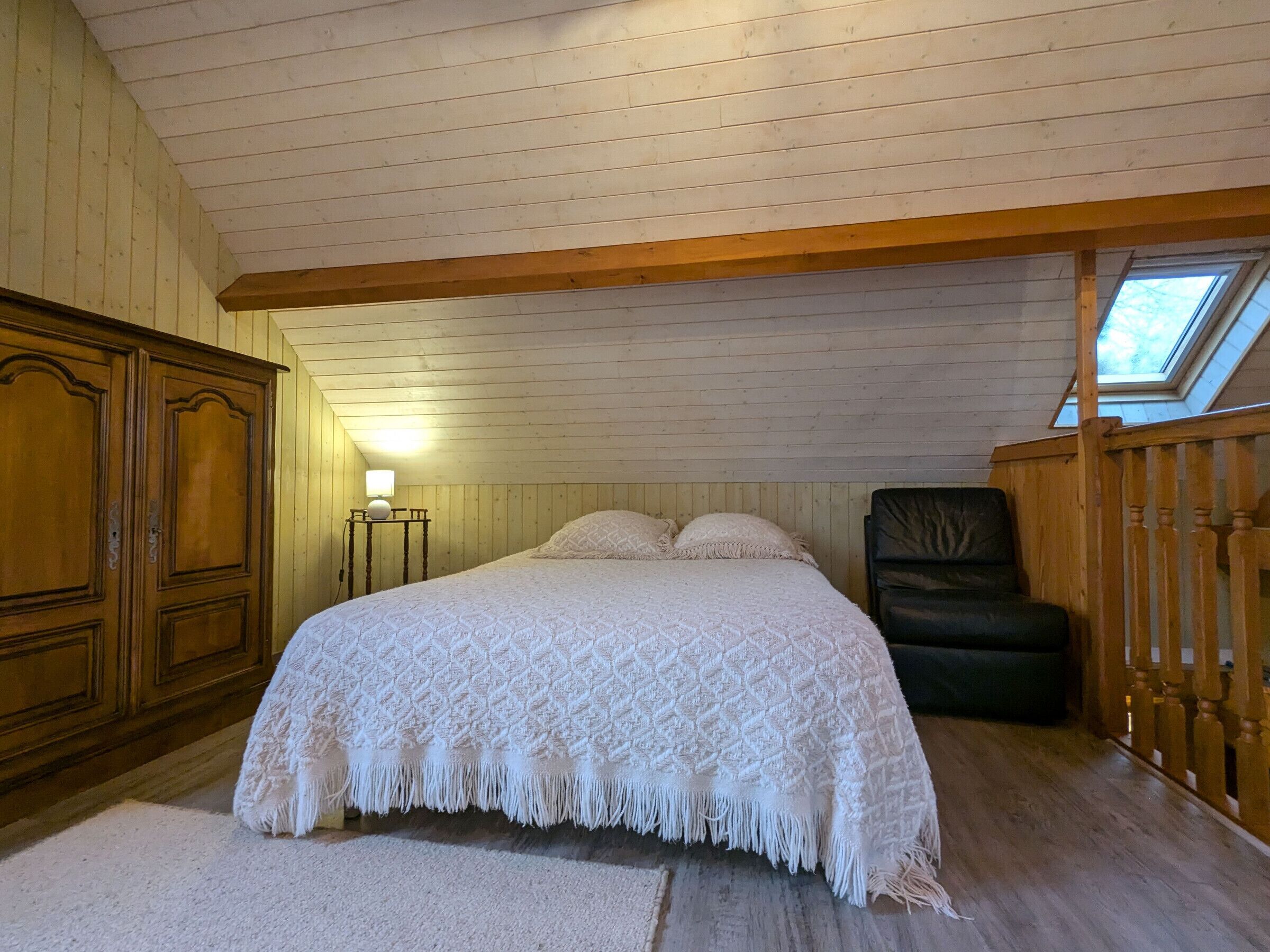 A bedroom with a large bed, a nightstand, a chair, and a skylight.