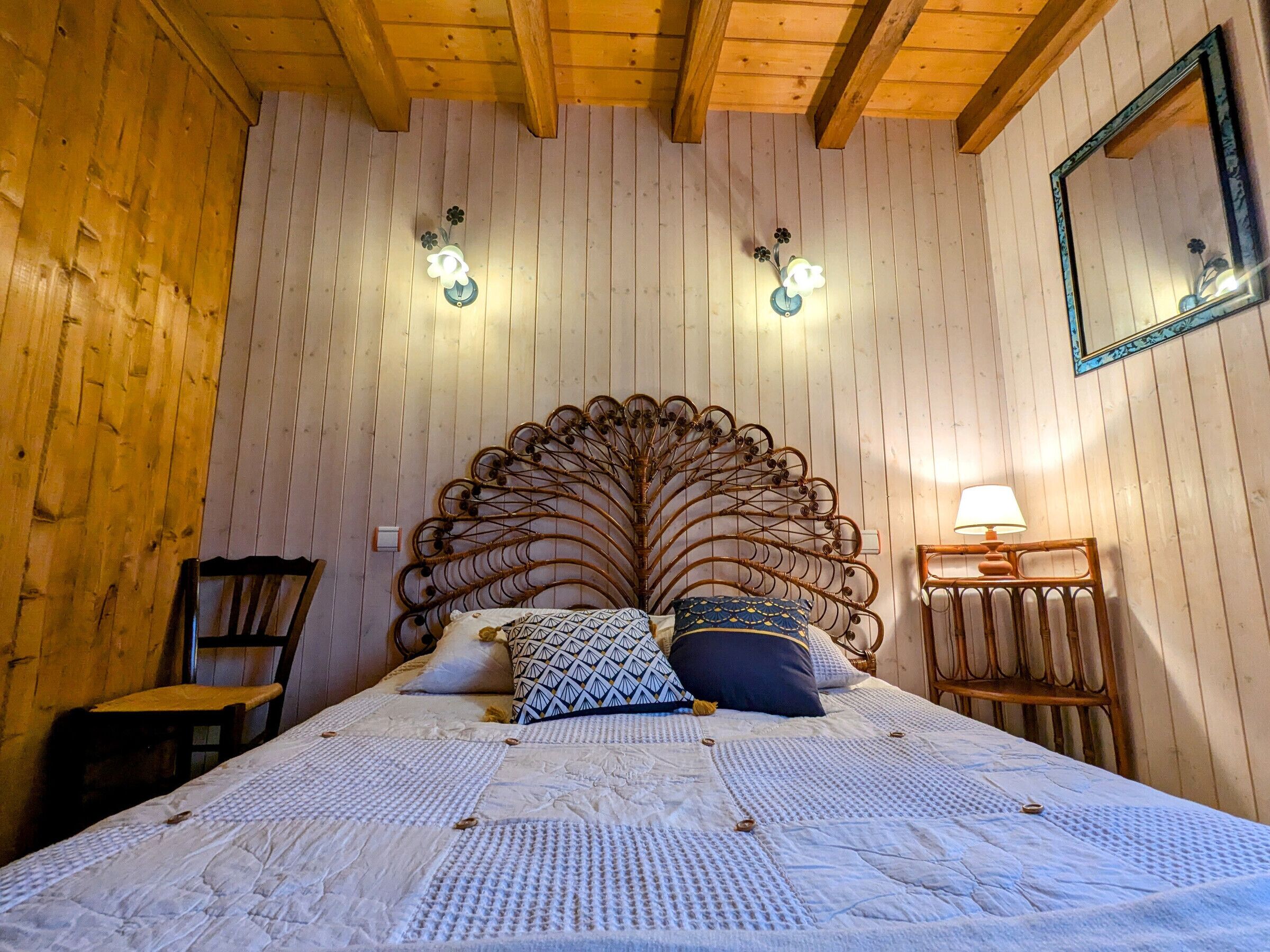 Una habitación con paneles de madera, una cama grande, dos apliques, un espejo y una mesita de noche con lámpara.