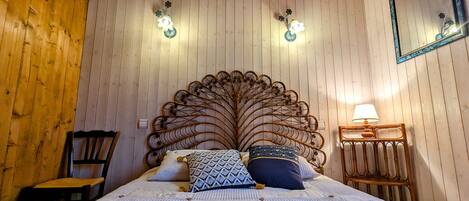 Una habitación con paneles de madera, una cama grande, dos apliques, un espejo y una mesita de noche con lámpara.
