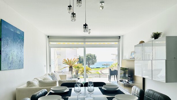 Un comedor moderno con una mesa grande preparada para cuatro personas, un sofá y vista al mar.