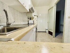A kitchen with a stainless steel sink, white cabinets, a microwave, and a tiled backsplash. - HORIZONTE AZUL. Frente al mar en la Playa de la Almadraba – Roses (Roses)