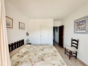 A bedroom with a bed, a chair, a wardrobe, and a door. - HORIZONTE AZUL. Frente al mar en la Playa de la Almadraba – Roses (Roses)