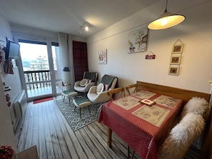 Una sala acogedora con una mesa de comedor, dos sillones, un sofá, un tapete estampado y un balcón con vistas.