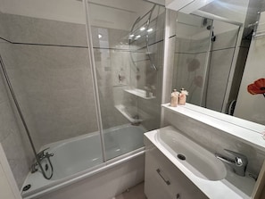 Un baño moderno con ducha envuelta en vidrio, un lavabo blanco y un espejo.