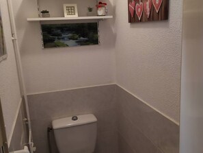 Un baño con inodoro, una repisa con adornos y una ventana pequeña.