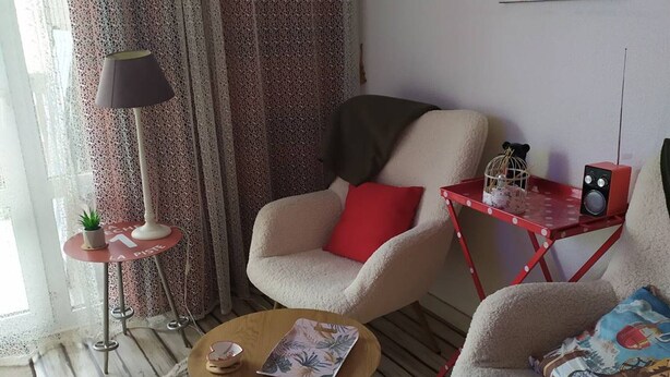 Un saló amb un sofà, una butaca, una taula de centre i una taula auxiliar vermella amb un altaveu.