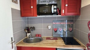 A compact kitchen with red cabinets, a microwave, a sink, and a small refrigerator. - Studio Les Saisies 4 people with balcony (Hauteluce)
