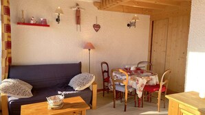 A cozy living room with a sofa, dining table, and chairs. There are wall decorations, a lamp, and a wooden ceiling. - Studio Les Saisies 4 people with balcony (Hauteluce)