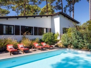 Une maison moderne avec une piscine, entourée de verdure et d’arbres.