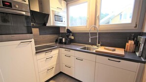 A modern kitchen with white cabinets, a stainless steel oven, a microwave, a coffee maker, and a sink. - Exklusives Skandinavisches Ferienhaus (Mirow)