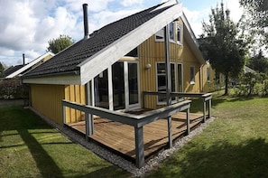 A wooden house with a sloped roof, large windows, and a deck.