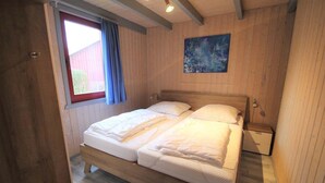 A wooden-paneled bedroom with a double bed, a window with blue curtains, and a painting on the wall. - Skandinavisches Ferienhaus in Mirow (Mirow)