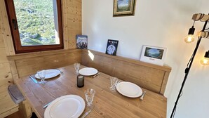 Et træspisebord dækket med tallerkener, glas og bestik, med udsigt til grønt uden for vinduet og et indrammet billede på væggen.