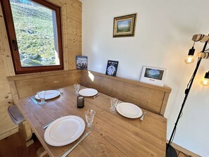 Un tavolo da pranzo in legno apparecchiato con piatti, bicchieri e posate, con vista su un paesaggio verde e un quadro appeso alla parete.
