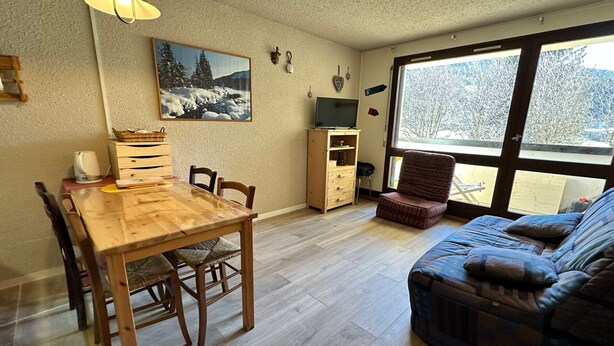 A cozy living room with a wooden dining table, a sofa, and a TV. - Studio for 4 pers at slopes' foot with south-facing balcony, parking (Corrençon-en-Vercors)