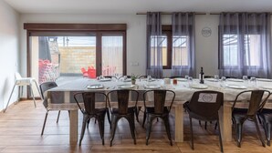 A dining area with a long table set for multiple people, chairs, and a view through a glass door to an outdoor area. - Country House 'Camino De Avila' with Mountain View, Private Pool and Wi-Fi (Mediana De Voltoya)