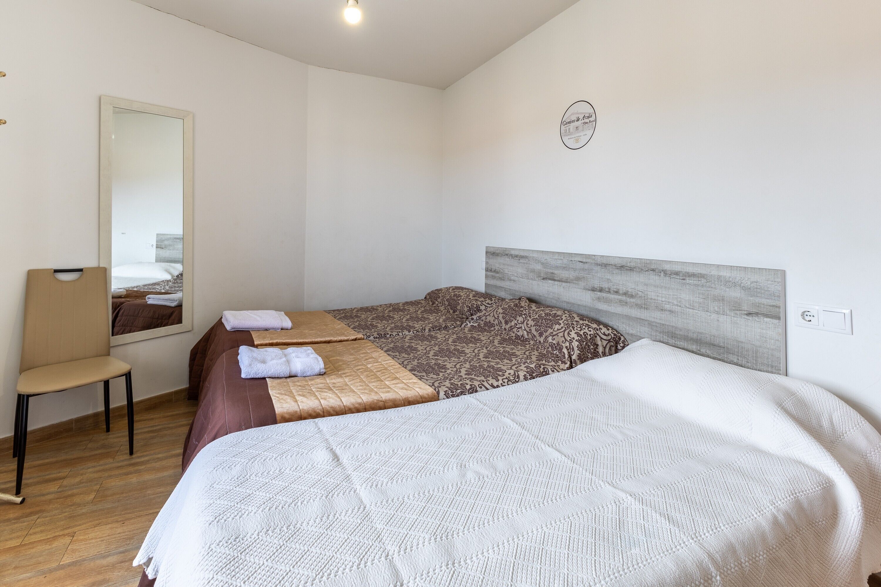 Una habitación de hotel con cama, una silla, un espejo y una lámpara fijada a la pared.
