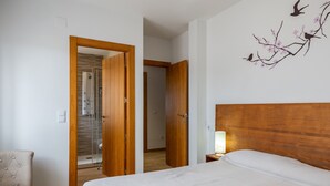 A bedroom with a bed, a chair, a wooden headboard, a wall art of birds and flowers, and a bathroom with a shower and toilet visible through an open door. - Country House 'Camino De Avila' with Mountain View, Private Pool and Wi-Fi (Mediana De Voltoya)
