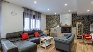 A living room with a stone wall, a fireplace, a sofa, a coffee table, and a dining area with red chairs. - Country House 'Camino De Avila' with Mountain View, Private Pool and Wi-Fi (Mediana De Voltoya)
