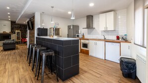 A modern kitchen with a central island, bar stools, a microwave, a dishwasher, and a stone accent wall. - Country House 'Camino De Avila' with Mountain View, Private Pool and Wi-Fi (Mediana De Voltoya)