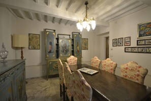 A dining room with a wooden table, floral-patterned chairs, a chandelier, and framed artwork on the walls. - Belvilla by OYO Villa Torreone (Cortona)