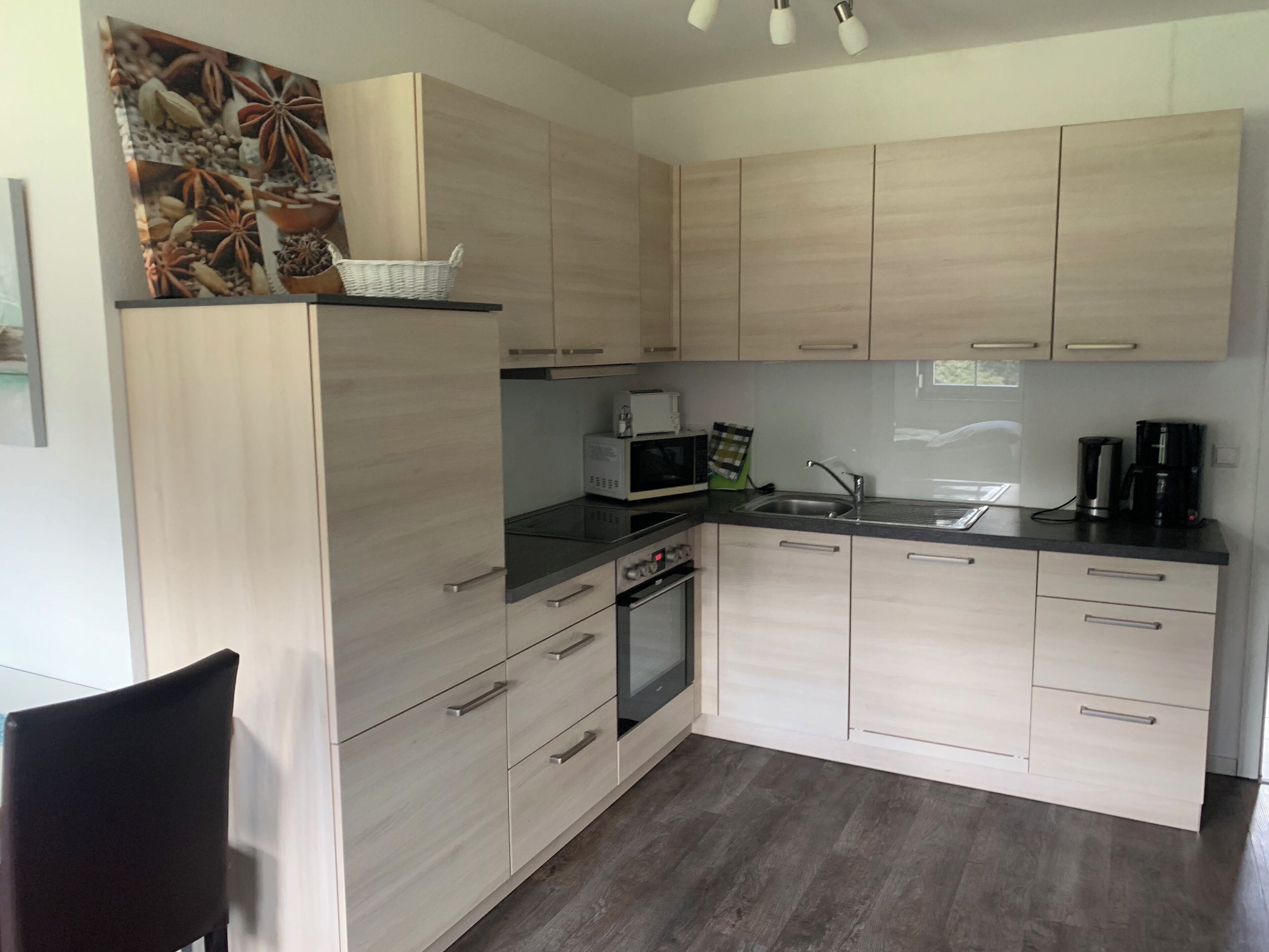 A modern kitchen with light wood cabinets, a microwave, a coffee maker, and a sink.