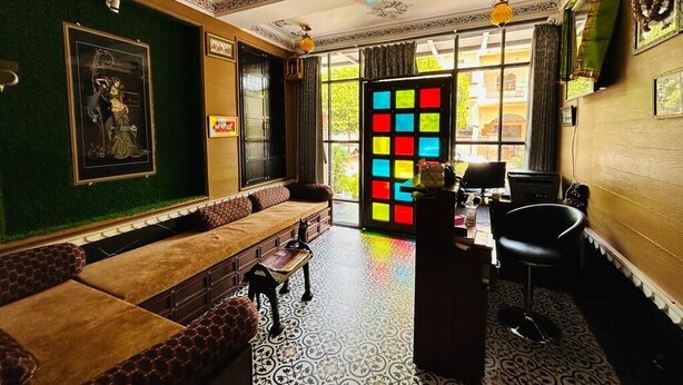 Ein Zimmer mit einem gemusterten Boden, einem Sofa, einem Schreibtisch und einem farbenfrohen Fenster.