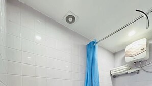 Ein Badezimmer mit weiß gefliesten Wänden, einem blauen Duschvorhang, einer Toilette, einem Waschbecken und einer an der Wand montierten Klimaanlage.