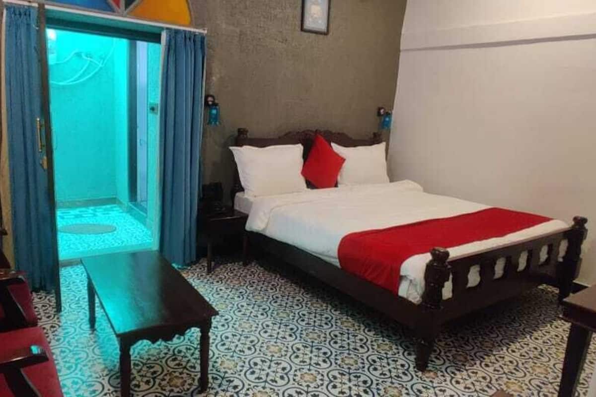 Une chambre d’hôtel avec un lit, un bureau et une chaise. Une porte donne accès à un balcon.