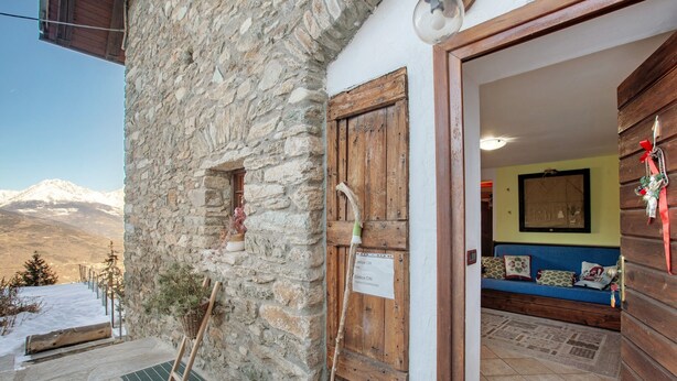 A stone building with a wooden door, a stone staircase, and a view of snow-covered mountains.