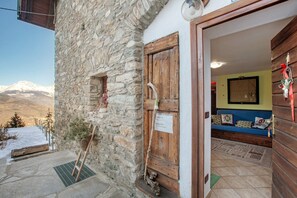 A stone building with a wooden door, a stone staircase, and a view of snow-covered mountains.
