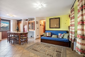 A living room with a sofa, a dining table with chairs, a patterned rug, and a framed picture on the wall.