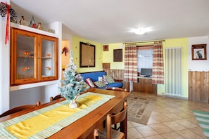 A dining area with a wooden table, chairs, a Christmas tree, and a blue sofa in the background.