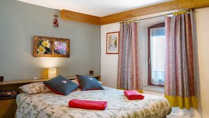 A bedroom with a bed, pillows, a nightstand, a lamp, a framed picture, and a window with curtains.