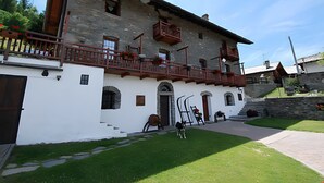 A two-story stone building with a balcony, a staircase, and a dog in the yard.