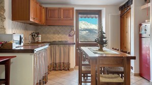 A kitchen with wooden cabinets, a dining table, chairs, a small Christmas tree, and a view of mountains through a window.