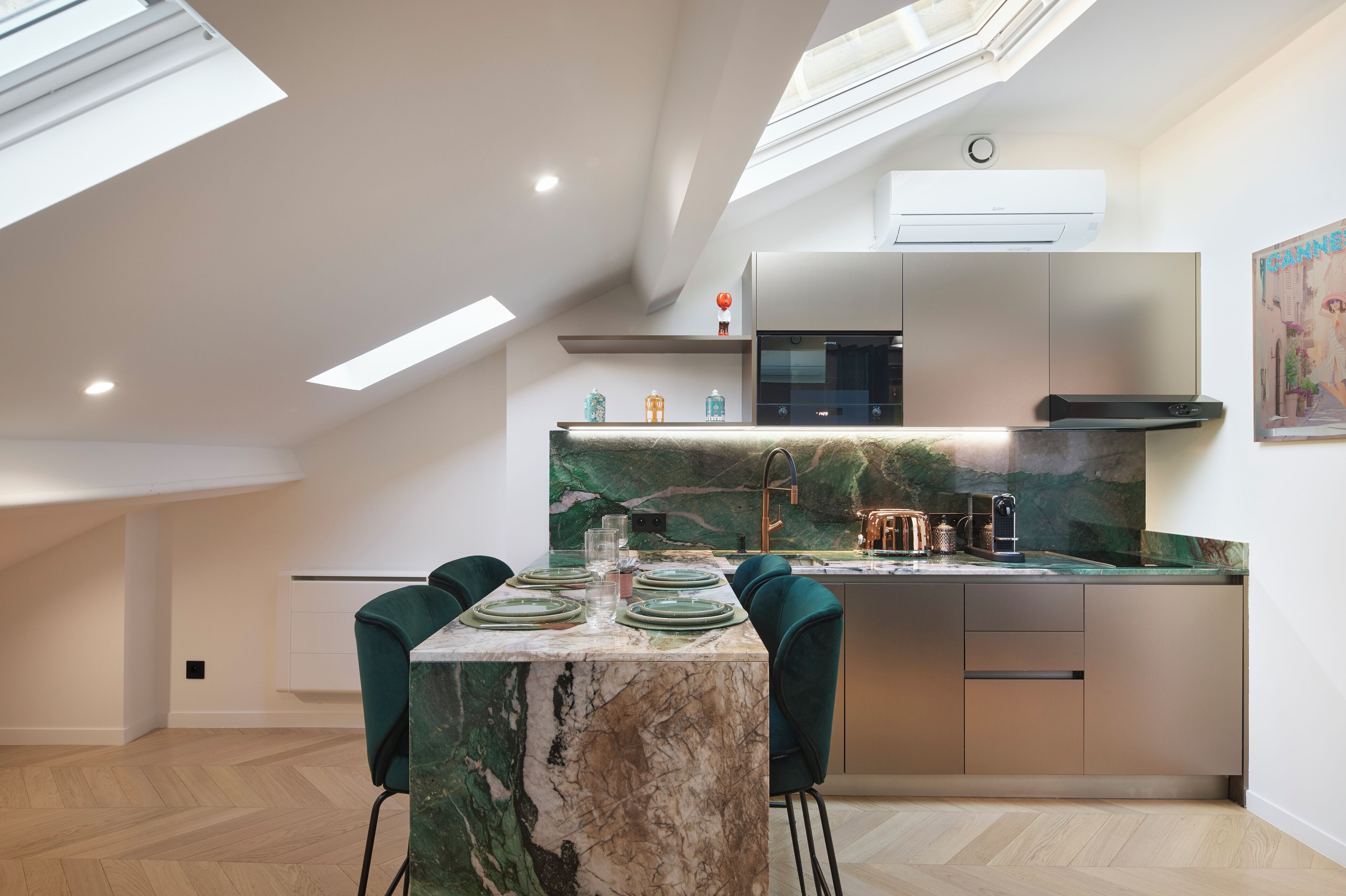 A modern kitchen with a marble countertop, green chairs, and a skylight.