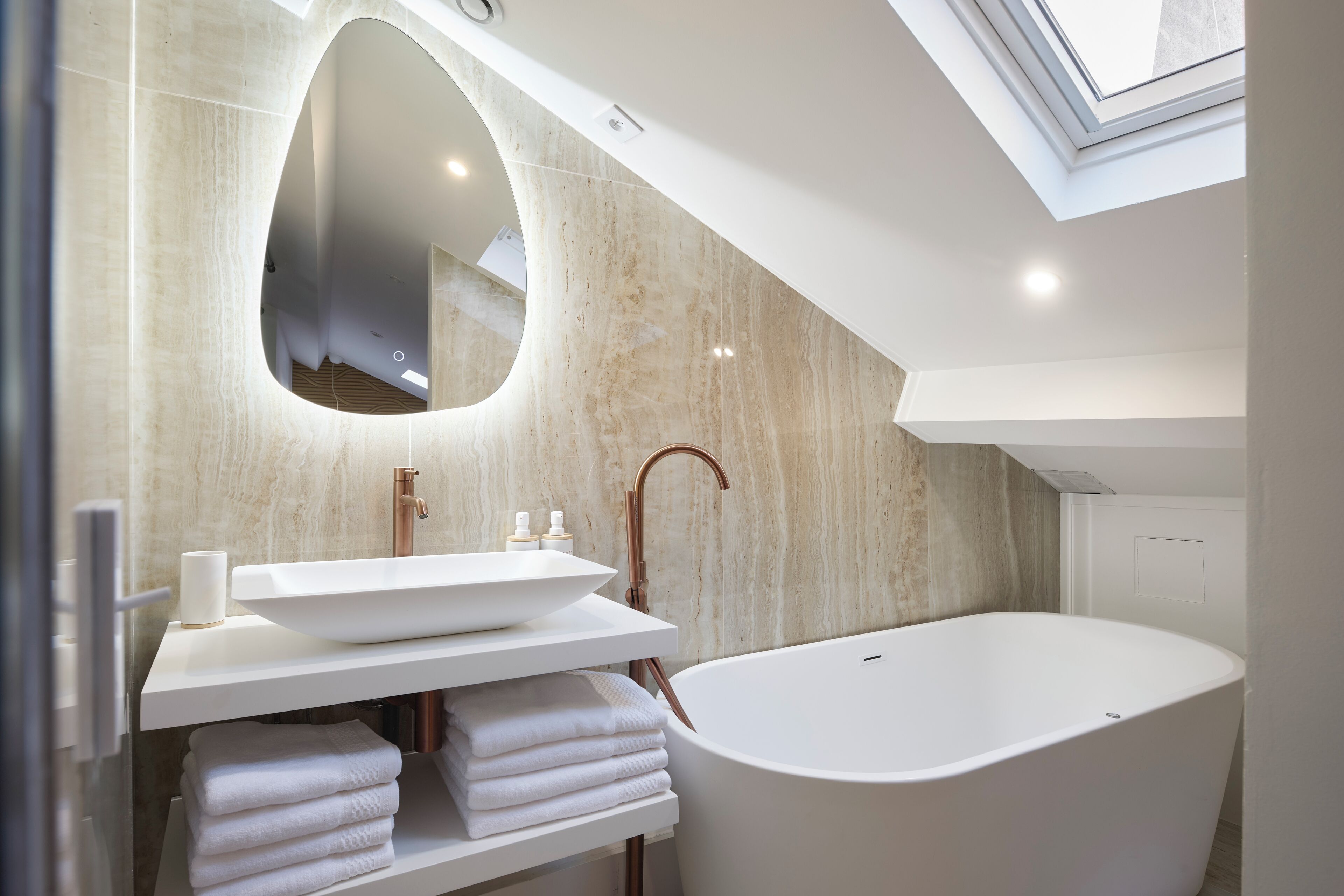 A modern bathroom with a freestanding bathtub, a large mirror, and a skylight.