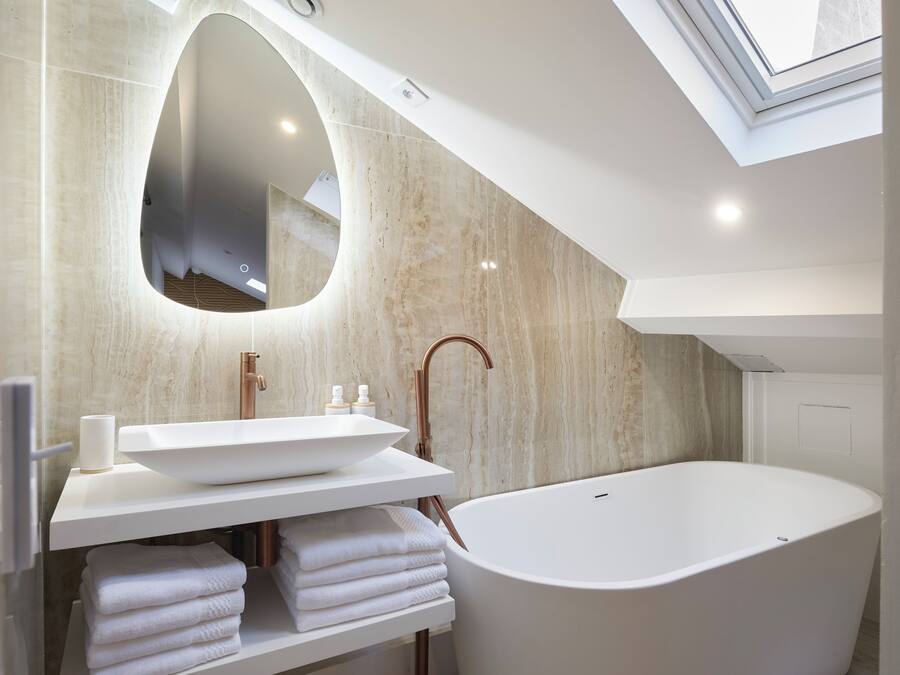 A modern bathroom with a freestanding bathtub, a large mirror, and a skylight.