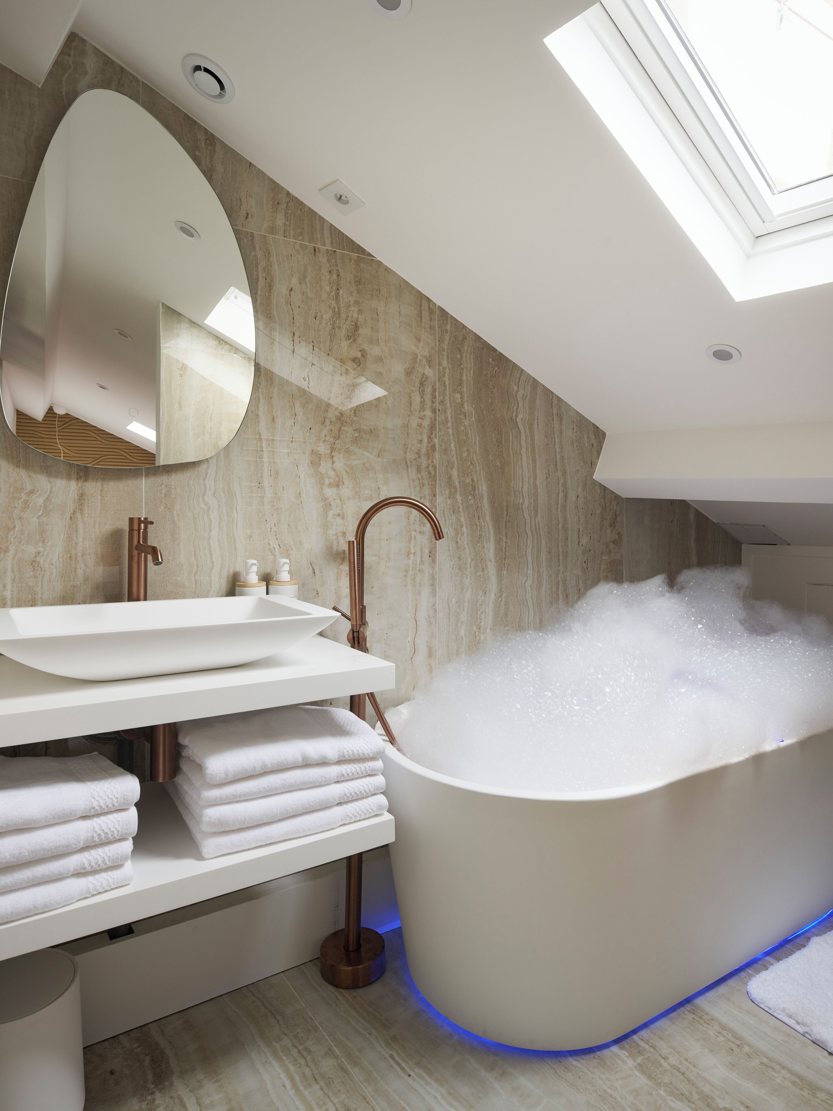A modern bathroom with a freestanding bathtub, a large mirror, and a white vanity with towels.
