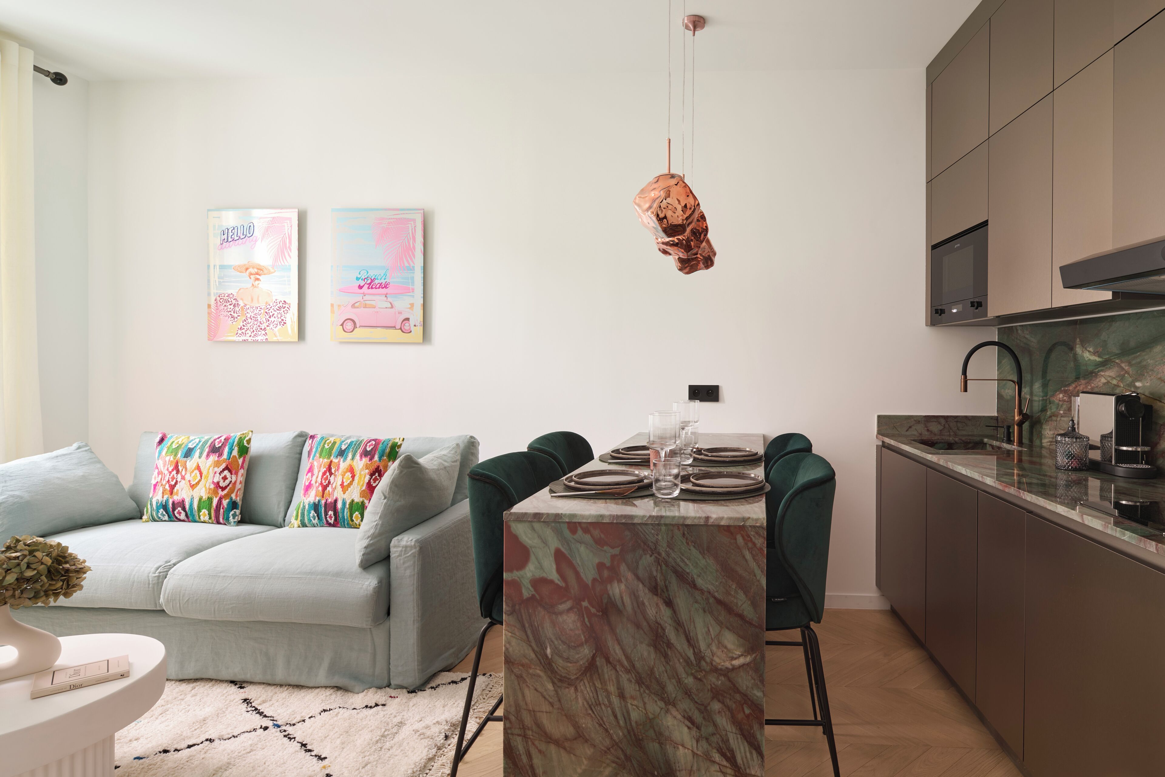 Een moderne keuken met een marmeren aanrecht, een eethoek met een tafel voor vier personen, en een grijze bank met kleurrijke kussens.