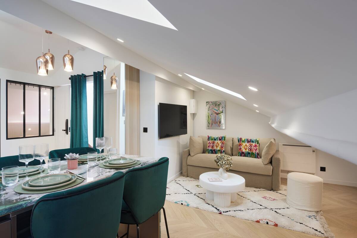 A modern dining area with a table set for four, a sofa, and a TV mounted on the wall.